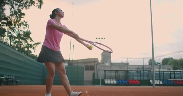 若い女性のテニス選手がテニスの試合を提供する準備のスローモーションで低角度ビュー。スポーツ練習中に女子アスリートがボールを強く打っている。業務用映像 — ストック動画
