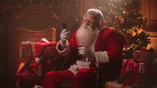 Merry Xmas time, Santa Claus is celebrating alone, listening to joyful song by smartphone in his residence house — Stock Video