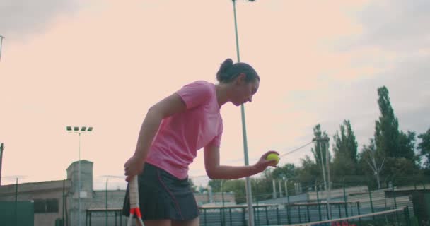 Αργή κίνηση: γυναίκα αθλήτρια κατά τη διάρκεια της πρακτικής της. Ένα κοντινό πλάνο μιας αθλήτριας που σερβίρει την μπάλα του τένις. Νεαρή γυναίκα χτυπάει την μπάλα με τη ρακέτα της στο ηλιοβασίλεμα. — Αρχείο Βίντεο
