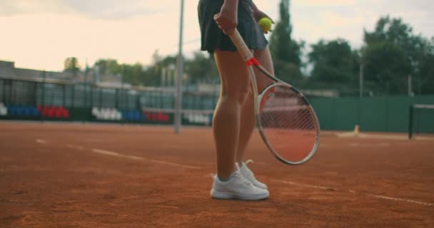 テニスをする女性の動きが遅い。スローモーション:テニスコートでボールを跳ねる女性のセクション。アスリートはテニスボールを提供します。若いです女性ありますヒットザボールとともに彼女のテニスラケットで日没 — ストック動画