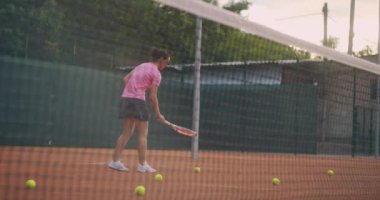 Dişi bir tenisçi sahada top toplar ve onları ağda kırar. Sahada bir kadın ve bir sürü dağılmış kılıç.