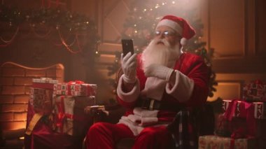 Noel Baba, akıllı telefondaki video konuşmalarıyla iletişim kuruyor. Noel gecesi evinde oturuyor.