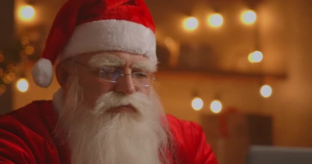 Papá Noel usando el portátil en la sala de estar. Retrato de Santa Claus reflexivo escribiendo con el ordenador portátil moderno en la casa decorada — Vídeos de Stock