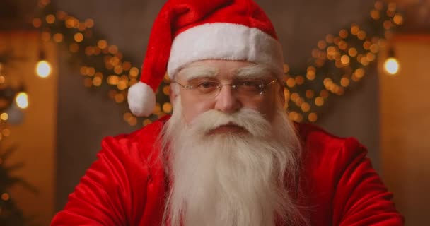 Detailní záběr šedovlasého Santa Clause v brýlích při pohledu do kamery. Hlavonosný portrét legračního starého vousatého Santa Clause. Svatý Mikuláš pozdrav na Veselé Vánoce — Stock video