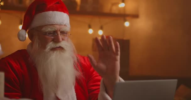 Skutečný Santa Claus pomocí nové technologie pro komunikaci s dětmi, příjem pošty nebo seznam přání. Veselý pracuje na notebooku a usmívá se, zatímco sedí u svého křesla s krbem a vánoční strom — Stock video
