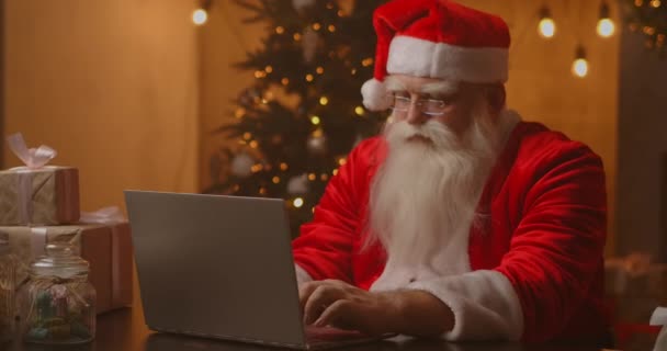 Jultomten använder laptop i vardagsrummet. Porträtt av omtänksam jultomten skriva med modern bärbar dator i dekorerat hus — Stockvideo