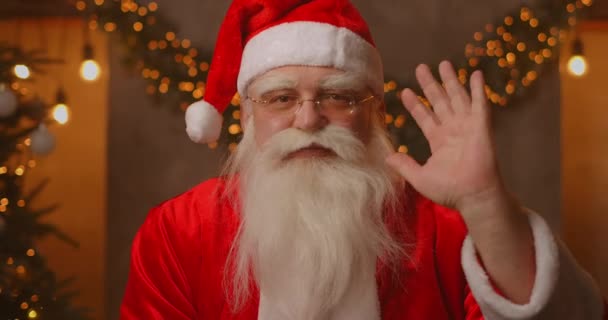 Headshot Looking at the camera Happy old bearded Santa Claus wearing costume and waving hand video calling in zoom, recording video Merry Christmas greeting, face camera view. — Stock Video