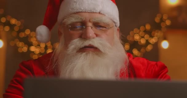 Papá Noel usando el portátil en la sala de estar. Retrato de Santa Claus reflexivo escribiendo con el ordenador portátil moderno en la casa decorada — Vídeo de stock