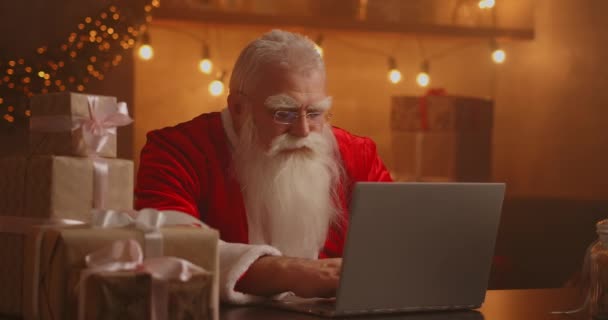 Papai Noel segurando caixa de presente digitando teclado garoto falando com a criança saudação no Feliz Natal, Feliz Ano Novo no bate-papo on-line virtual no laptop sentado à mesa em casa tarde com presente na véspera de Natal. — Vídeo de Stock