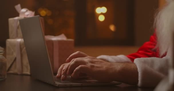 Manos Santa mecanografía en el teclado inalámbrico por mesa decorada de madera Año Nuevo, Santa Claus está trabajando con un ordenador portátil mirando a través del correo y respondiendo a los mensajes a los niños. — Vídeo de stock