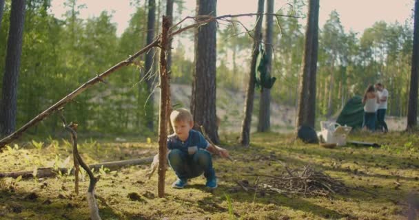 Сімейна поїздка в мальовничому лісі влітку, подружня пара штовхає намет, і маленький хлопчик грає — стокове відео