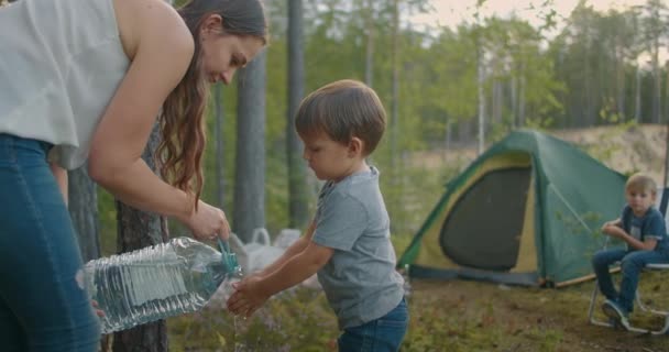 Ребенок моет руки в лесном походе, мать наливает воду из бутылки, семейный лагерь в резерве на выходные — стоковое видео