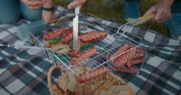 Picknick in de natuur, mensen grillen worsten op het rooster, nemen gebakken worst door handen en mes, close-up uitzicht — Stockvideo