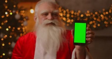 Noel Baba parmağını yeşil ekran cep telefonu ekranına doğrultuyor. Noel indirimi. Yaşlı Noel Baba kromatonlu bir ekran gösterir