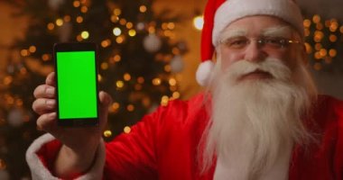 Noel Baba parmağını yeşil ekran cep telefonu ekranına doğrultuyor. Noel indirimi. Yaşlı Noel Baba kromatonlu bir ekran gösterir