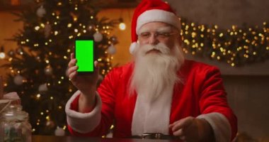 Noel Baba parmağını yeşil ekran cep telefonu ekranına doğrultuyor. Noel indirimi. Yaşlı Noel Baba kromatonlu bir ekran gösterir