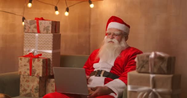 Santa Claus video ringer tak till barn på laptop hålla närvarande sitta hemma bord. Pandemin och tomtens isolering gratulerar barn på distans — Stockvideo