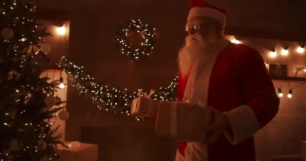 クリスマスの夜、サンタは誰もが眠っている間に家に贈り物を届けます。サンタは装飾された家のクリスマスツリーの下に贈り物を残します — ストック動画
