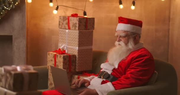 Santa Claus videollamadas tak a niño en portátil mantenga presente sentarse en la mesa de casa. La pandemia y el aislamiento del Santa felicita remotamente a los niños — Vídeos de Stock