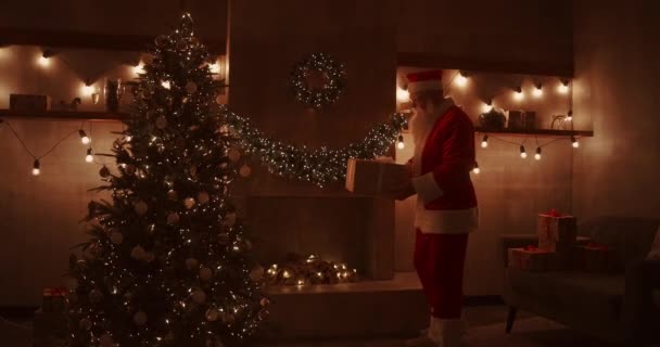 Santa Claus trae regalos bajo el árbol de Navidad para niños. Dar regalos a los niños en la noche de Navidad. Santa pone un regalo bajo el árbol de Navidad — Vídeos de Stock