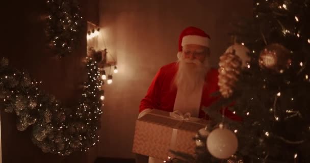 Święty Mikołaj przynosi prezenty pod choinkę dla dzieci. Prezenty dla dzieci w Wigilię. Mikołaj kładzie prezent pod choinkę — Wideo stockowe