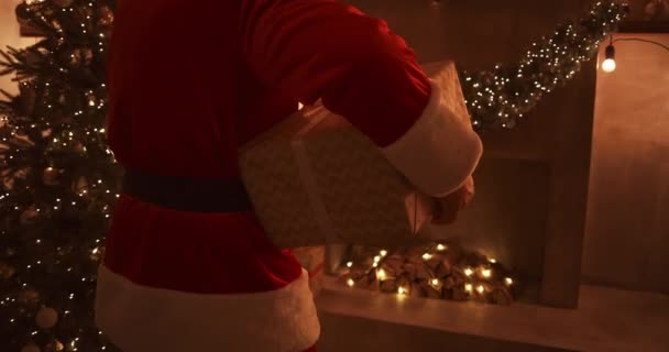 Cerca - hasta de la mano de Santa: trae regalos bajo el árbol de Navidad para los niños. Dar regalos a los niños en la noche de Navidad. Santa pone un regalo bajo el árbol de Navidad — Vídeo de stock