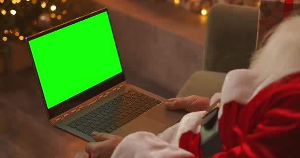 Pendant la quarantaine, le Père Noël félicite les enfants en utilisant un lien vidéo. Écran vert de l'ordinateur portable sur les genoux du Père Noël. Vue arrière d'un écran d'ordinateur portable avec un chrome sur le fond — Video