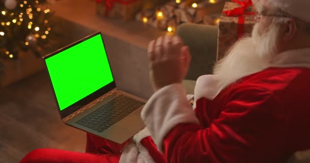 Le Père Noël parle sur un appel vidéo via un ordinateur portable. Utilisez l'écran vert pour un appel vidéo. Père Noël salue avec sa main en regardant l'écran vert de l'ordinateur portable — Video