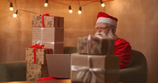 Santa Claus βίντεο καλώντας tak στο παιδί στο φορητό υπολογιστή κρατήστε πατημένο το παρόν κάθονται στο σπίτι τραπέζι. Πανδημία και απομόνωση του Αϊ Βασίλη συγχαίρει εξ αποστάσεως τα παιδιά — Αρχείο Βίντεο