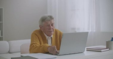 Laptop bilgisayarı olan yaşlı bir kadın akıllı telefondan evden arıyor. Yaşlı bir kadın, rahat bir dairede dizüstü bilgisayarında gülümseyen ve mutlu bir şekilde konuşan bir video görüşmesi yapıyor. Doktor videosu yaşlı hastayı arıyor