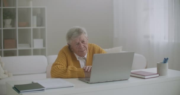 Mulher velha conversa com sua neta em videochamada usando um laptop.Video conferência com um médico — Vídeo de Stock