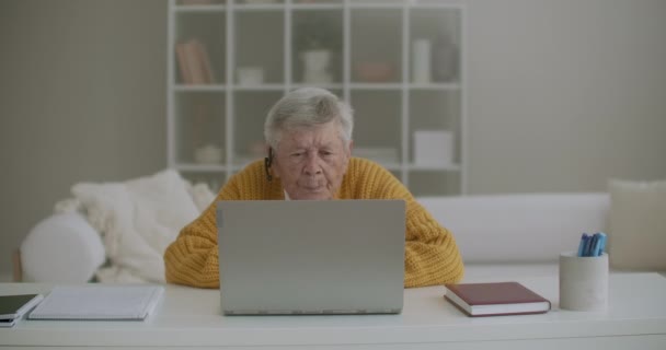 Oudere vrouw met grijs haar maken videogesprek met behulp van laptop thuis. Oudere vrouw die een videogesprek heeft met familie, glimlachend en zwaaiend. COVID 19 Blijf verbonden. Online chatten met vrienden — Stockvideo