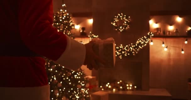 Santa trae un regalo a los niños en la noche de Navidad y lo pone cerca del árbol de Navidad en la casa de los niños. la cámara monitorea la entrega del regalo bajo el árbol — Vídeo de stock