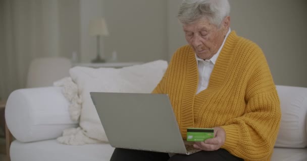 Compras en línea y el concepto de la gente - mujer mayor feliz con ordenador portátil y tarjeta de crédito o bancaria en casa. Anciana de compras con tarjeta de crédito y portátil — Vídeos de Stock