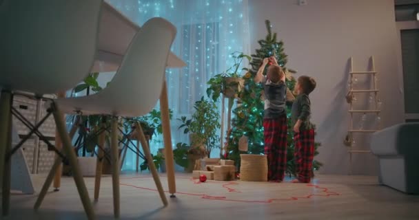 Deux frères en pyjama décorent le bal de Noël dans le salon de la maison la veille de Noël — Video