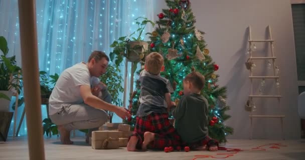 Una familia con dos hijos decoran un árbol de Navidad en Nochebuena. El padre y la madre con los niños se preparan para el año nuevo y la casa de decoración de Navidad — Vídeo de stock