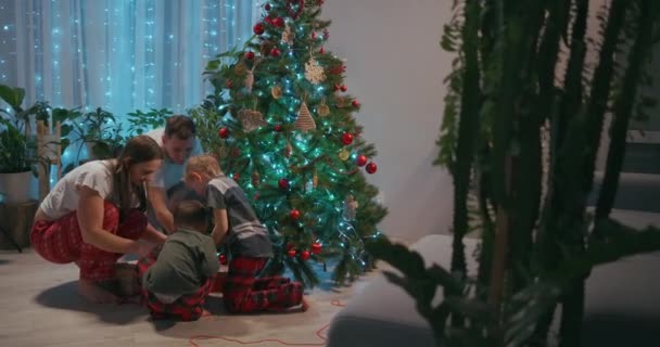La familia decora el árbol de Navidad juntos. El padre es una madre y dos hijos se ponen en los árboles de Navidad juntos. Familia feliz en Nochebuena — Vídeo de stock