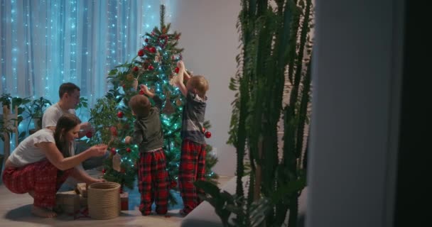 Šťastná rodina se připravuje na Silvestrovské zimní svátky koncepce oslav. Mladí 30s pár jeho předškolní rozkošný dva synové zdobení vánoční stromeček vytvořit slavnostní atmosféru v moderním útulný — Stock video