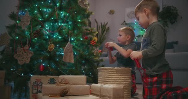 Twee jongens versieren kerstboom kerstboom in de woonkamer met kerstspeelgoed. Voorbereiding van het nieuwe jaar en Kerstmis — Stockvideo