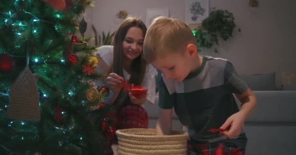 El niño selecciona bolas de vidrio para que su madre decore el árbol de Navidad. La familia decora el hogar juntos para Navidad — Vídeos de Stock