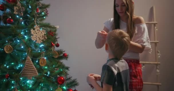 Mamma e suo figlio appendono giocattoli dell'albero di Natale in cima all'albero di Natale — Video Stock