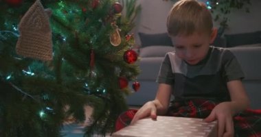  Mutlu Gülümseyen Küçük Çocuk Noel hediyesini Noel Baba 'dan açıyor. Çocuk Noel hediyesini evde açıyor..