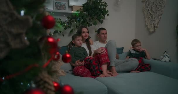 Семья из трех человек - отец, мать и буксир сына смотрят телевизор по вечерам. Сплоченность, карантин, остаться дома — стоковое видео