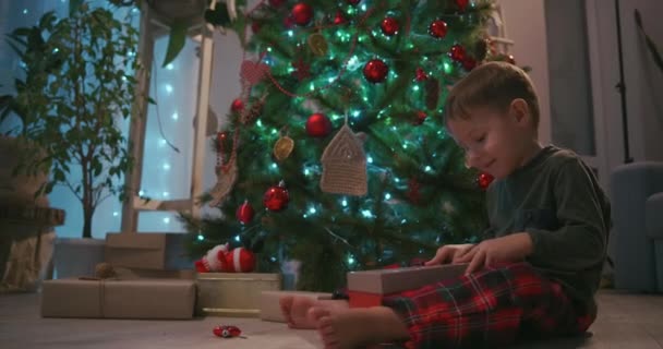 Çocuk hediyeyi açar ve kutudan gelen ışık neşeli yüzü aydınlatır. Ağacın altındaki hediyeyi aç. — Stok video