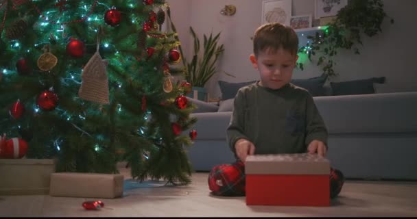 Gelukkig glimlachend jongetje opent zijn kerstcadeau van de kerstman. jongen opening kerstcadeau thuis. — Stockvideo