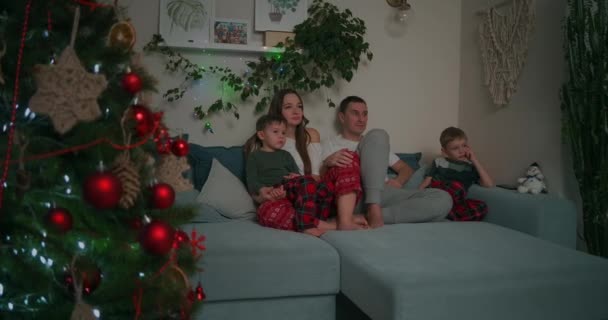 三个孩子的家人- -父亲、母亲和两个儿子晚上看电视.团结，隔离，待在家里 — 图库视频影像