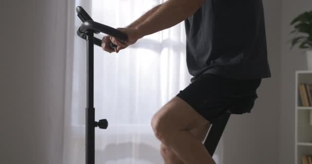 Ενήλικος αθλητής είναι η κατάρτιση σε σταθερό ποδήλατο στο σπίτι, closeup του σώματος, φροντίδα για την υγεία, διατήρηση σε φόρμα — Αρχείο Βίντεο