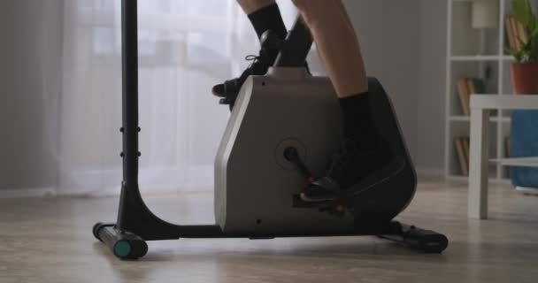 Modern, helyhez kötött kerékpár otthoni edzéshez, közelkép férfi lábakról pedálon, fizikai és sportos tevékenységek — Stock videók