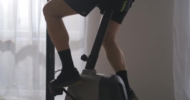Pernas de homem magro e envelhecido treinando em bicicleta estacionária no quarto, visão de close-up, perder peso e manter a condição física — Vídeo de Stock