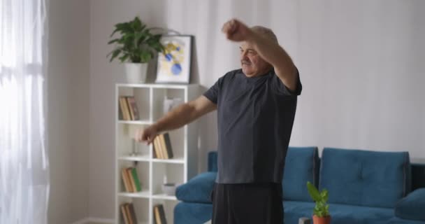 Dorosły mężczyzna trenuje w domu rano, podnosząc ręce naprzemiennie, zdrowy tryb życia w średnim wieku — Wideo stockowe